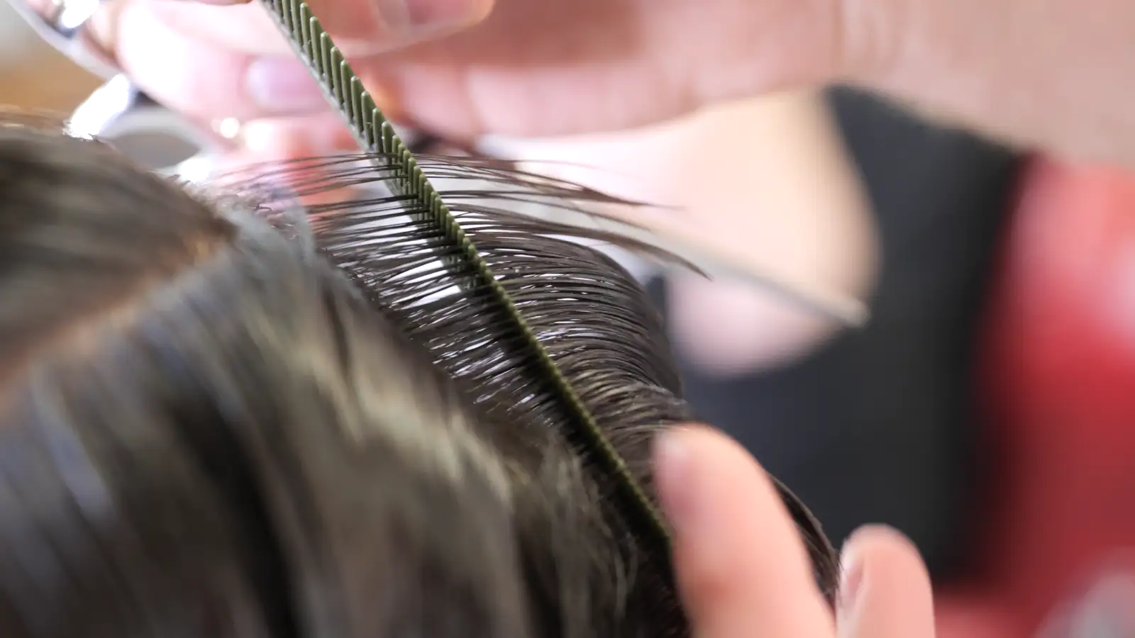A comb drawing a section of wet hair straight before the cut