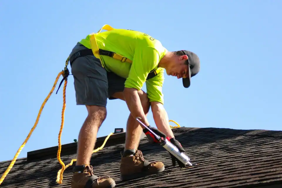 A Ridgeline roofer tied off and working on a shingle roof under a blue sky