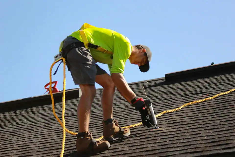 A roofer in a high-vis shirt sealing a shingle roof